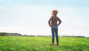 Girl standing with hands on hips and Relay in back pocket, looking out into the distance over a green field