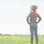 Girl standing with hands on hips overlooking a field with a Relay in her back pocket