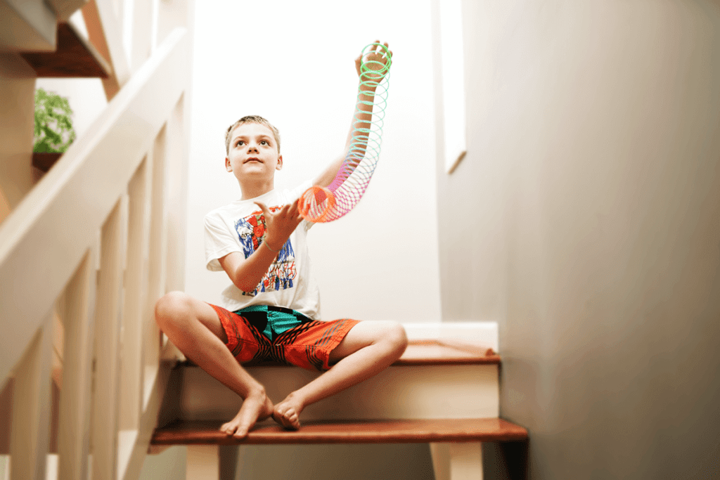 Child sitting at top of stairs stretching out a rainbow-colored Slinkie