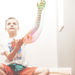 Child sitting at the top of stairs holding an outstretched rainbow-colored Slinkie