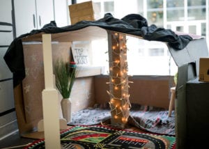 cardboard fort with string lights, homemade props, a chimney, and a blanket door