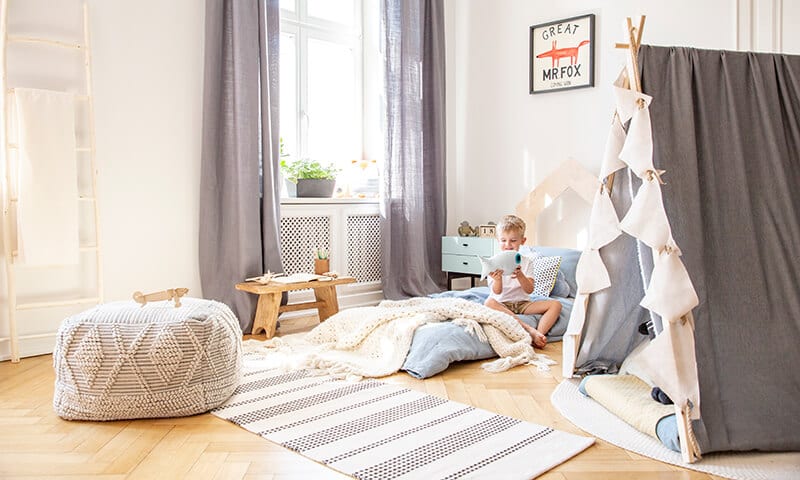 boy sitting on blankets and pillows in a stylish playroom with a tent and a large window